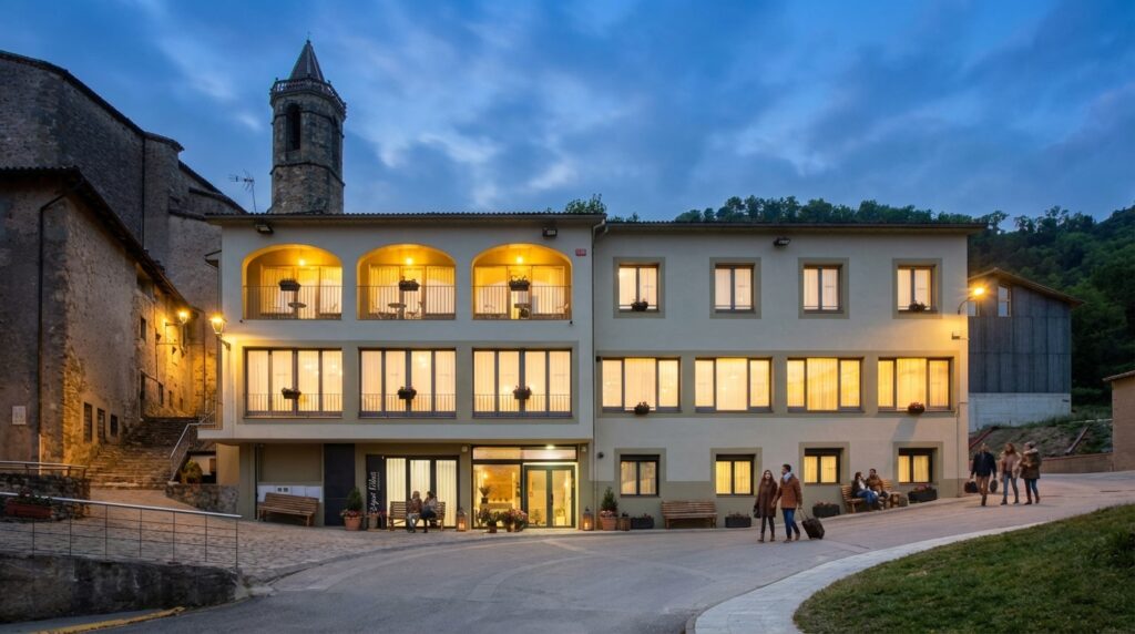 Fotografía en plano general de la histórica fachada de piedra de la Masía Espai Vidrà, con la suave y clara luz de la mañana iluminando las vigas y los balcones restaurados a mano. Nota Columna única (galería).